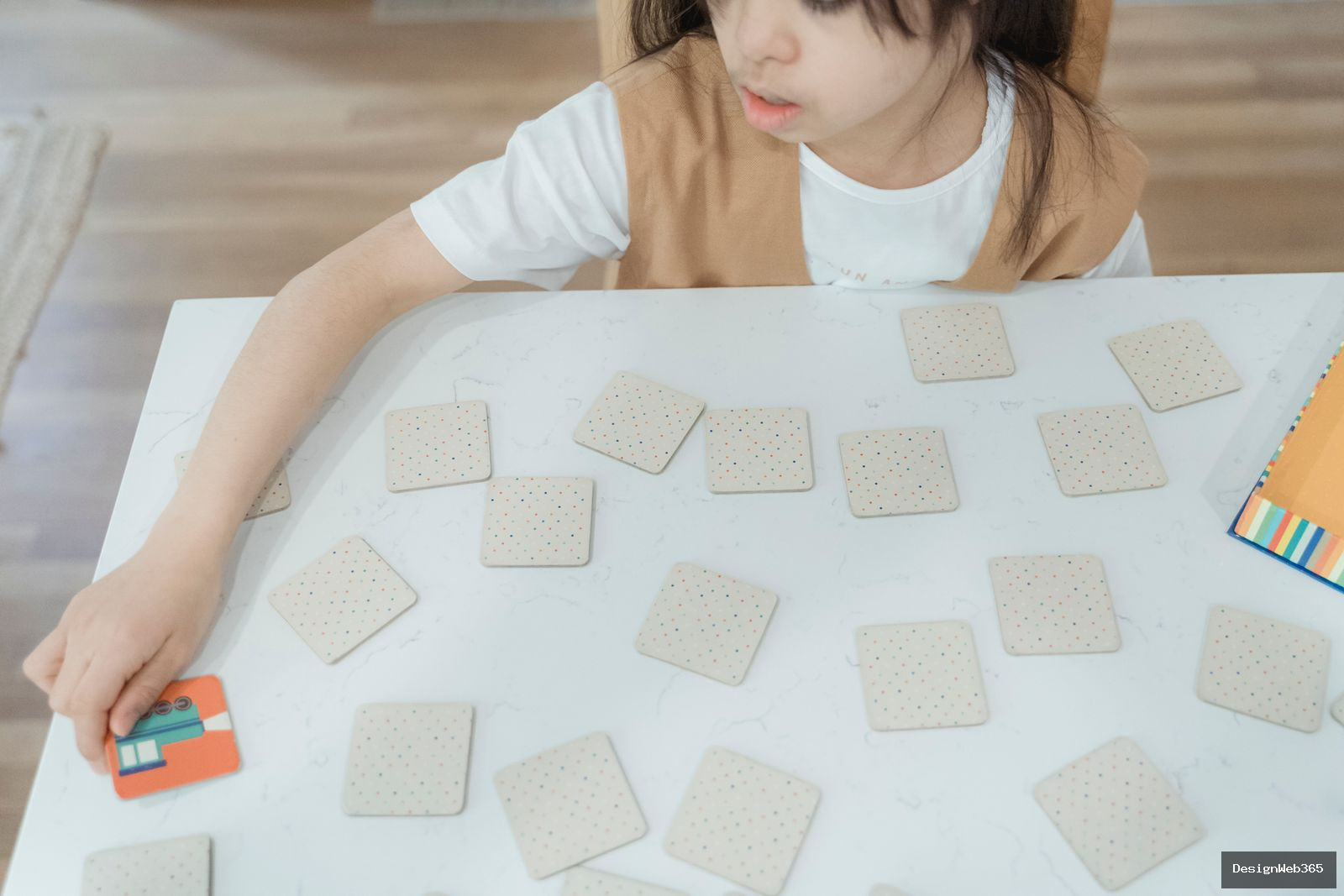 Vue de dessus d'un enfant jouant a un jeu de memoire avec des cartes disposees sur une table