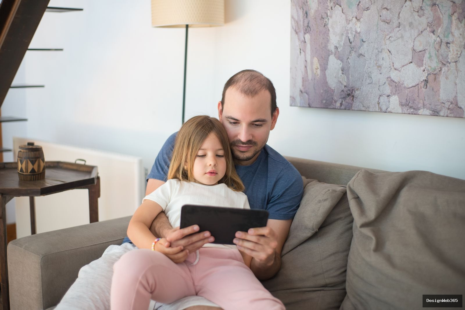 Pere et fille regardant ensemble une tablette sur un canape